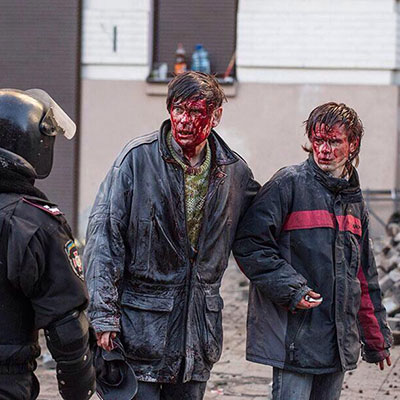 A man and a boy, their faces covered in blood, look aghast at a riot policeman on a street in kiev, early 2014.